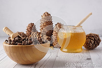 Pine nuts in a bowl and honey in a glass pot on a light background next to cedar cones Stock Photo