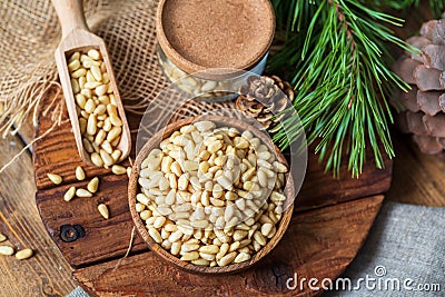 Pine nuts in a bowl, pine cone, branch, glass jar on a cutting board. Still life from natural ingredients, top view. Stock Photo