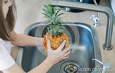 Pineapple being cleaned and washed in a kitchen sink. Wash food. Child hands holding tasty fresh pineapple. Healthy lifestyle. Stock Photo