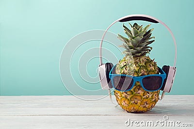 Pineapple with headphones and sunglasses on wooden table over mint background. Tropical summer vacation and beach party. Stock Photo
