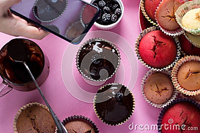 On a pink background a woman`s hand shoots cupcakes on a smartphone camera with chocolate and berries Stock Photo