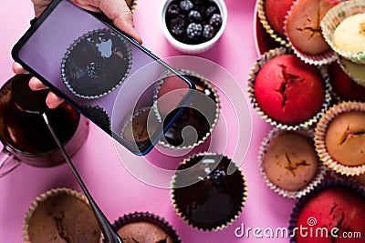 On a pink background a woman`s hand shoots cupcakes on a smartphone camera with chocolate and berries Stock Photo