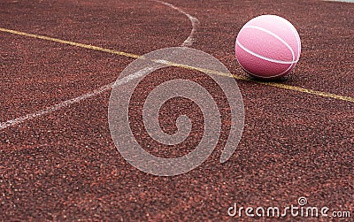 Pink basketball ball on the ground. Close-up ball on the red court. Basketball on the street or indoor court. Stock Photo
