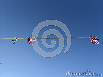 Pink and blue clothes pegs hanging on a yellow washing line in the sky Stock Photo