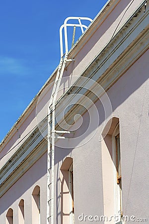 Pink building with metal saftey roof access ladder on blue sky with clouds background in midday sun or late afternoon Stock Photo