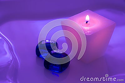 A pink burning candle with glass blue pebbles. Candle for spa salons. Purple toning. Stock Photo