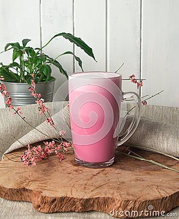 Pink coffee latte macchiato in a glass cup on a wooden backing decorated with dried flower Stock Photo