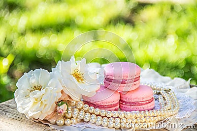 Pink delicate macaroons and white roses. Women`s sweets. Sweet gift. Exquisite dessert. Stock Photo