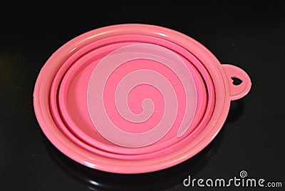 Pink folding and multifunctional rubber plate, a bowl with a plastic edging on a black glossy surface. Stock Photo