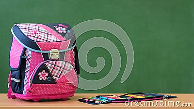 Pink girly school bag and pencil case on a desk against green board. First day of school. Stock Photo