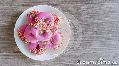 Pink glazed mini donuts in white plate on wooden table. Sweet food background Stock Photo