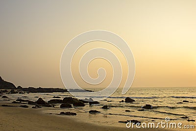 A pink gray clear sunset sky over the sea against a sandy beach with rocks in the ocean Stock Photo