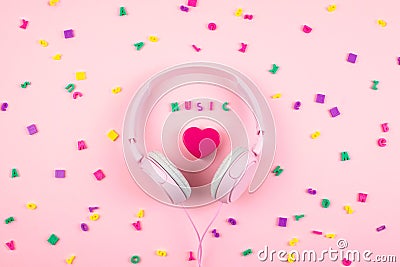 Pink headphones and heart with word MUSIC and multicolored letter symbols on pink background. Minimal Music concept. Top view. Stock Photo