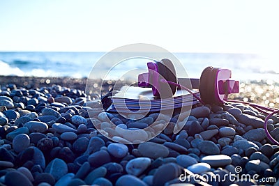 Pink headphones lying at paper notebook on sea beach Stock Photo