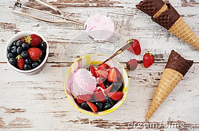 Pink Ice Cream served with berries - strawberries and blueberries in a yellow bowl. Waffle cones with chocolate. Light Rustic Wood Stock Photo