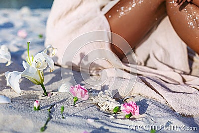 Pink lilies lying on sand foreground and young beatiful woman legs at background on the beach at sunset Stock Photo