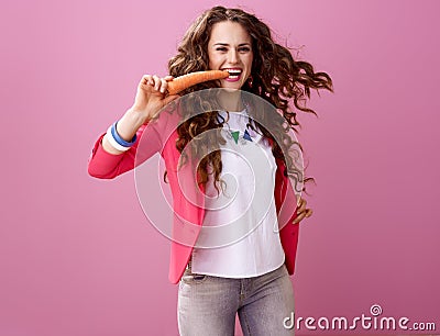 Cheerful stylish woman on pink background eating carrot Stock Photo