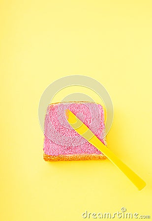 Pink neon color smeared on a piece of bread on a yellow background. The yellow knife is on the bread. Creative food concept, Stock Photo