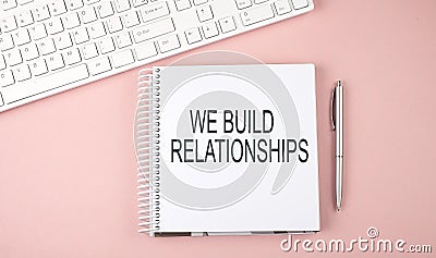 Pink office desk with keyboard and notebook with text WE BUILD RELATIONSHIPS Stock Photo