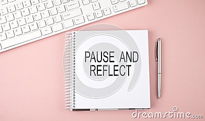 Pink office desk with keyboard and notebook with text PAUSE AND REFLECT Stock Photo