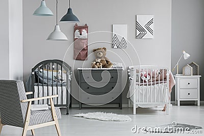 Pink organizer on wall of trendy baby bedroom with two cribs and chest of drawers Stock Photo