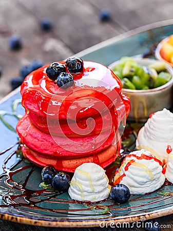 Pink pancakes with honey, chocolate, jam, whipped cream, berries and fruits on plate. Stock Photo
