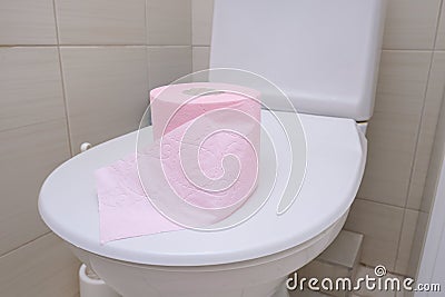 A pink piece of toilet paper standing on a cover of a toilet bowl, digestive problems and defecation disorder concept Stock Photo