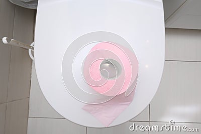 A pink piece of toilet paper standing on a cover of a toilet bowl, top view, digestive problems and defecation disorder concept Stock Photo