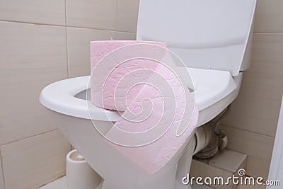 A pink piece of toilet paper standing on a seat of a toilet bowl, digestive problems and defecation disorder concept Stock Photo