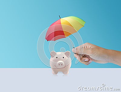 Pink piggy ceramic bank with colorful rainbow umbrella, insurance Stock Photo