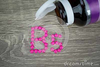 Pink pills forming shape to B5 alphabet on wood background Stock Photo