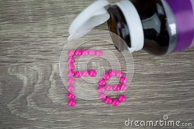 Pink pills forming shape to Fe alphabet on wood background Stock Photo