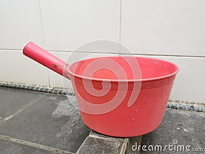 Pink plastic gayung or bucket, scoop, bailer,water dipper on the toilet floor. Stock Photo