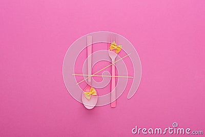 Pink plastic spoon upside down and fork, spaghetti and two uncooked macaroni isolated on pink. Stock Photo