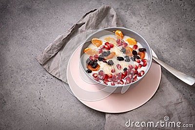 plate of oatmeal porridge with fruit slices, tangerine slices, raisins, dried apricots, pomegranate seeds on a gray background, Stock Photo