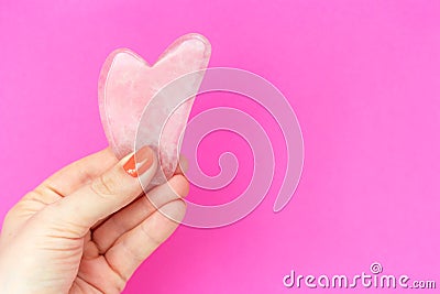 Pink quart guasha in woman`s hand on background a copy space Stock Photo