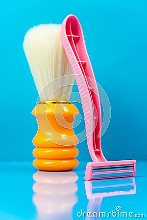 Pink razor stands with an orange shaving brush on a blue background Stock Photo