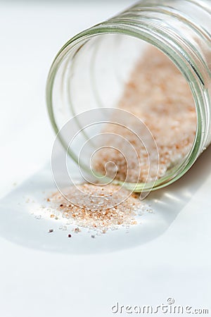 pink salt spill from small glass container on white background Stock Photo