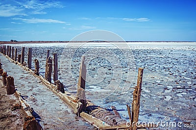 Pink salty lake with path, hedged by weathered old wooden sticks Stock Photo