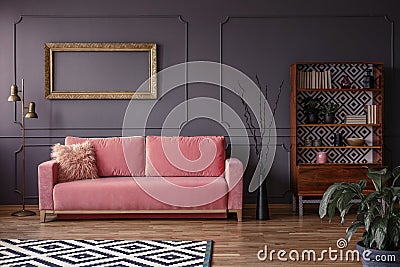 Pink settee against grey wall with mockup of gold frame in elegant living room interior. Real photo Stock Photo