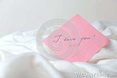 A pink sheet of paper with the words `I love you` on white crumpled fabric Stock Photo