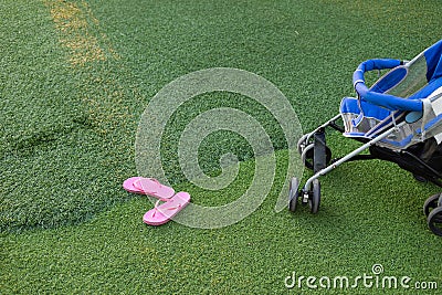 Pink slipper and part of baby stroller on green grass Stock Photo