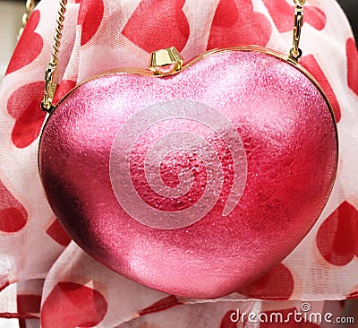 Pink sparkly heart purse with a gold chain strap hanging in front of a red heart print scarf Stock Photo