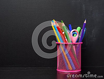 pink stationery glass with multi-colored wooden pencils and pens black chalkboard background Stock Photo