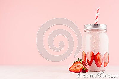 Pink strawberry smoothie with piece juicy fruit in retro jar with red striped straw on light soft pastel pink wall and white wood. Stock Photo