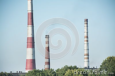 The pipes of the plant rise above the forest. Industrial landscape. Harmful environmental production. Environmental pollution. Stock Photo