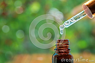 Pipette with essence drop and bottle, closeup on blurred nature background. Herbal essential massage oil dripping into Stock Photo