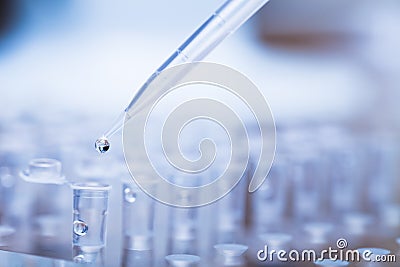 Pipette tip with droplet over rack of test tubes Stock Photo