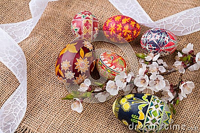 Pisanki with cherry blossom and white ribbon on sackcloth. Easter eggs in ethnic style. Easter eggs on canvas. Stock Photo