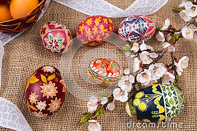 Pisanki with cherry blossom and white ribbon on sackcloth. Easter eggs in ethnic style. Easter eggs on canvas. Stock Photo